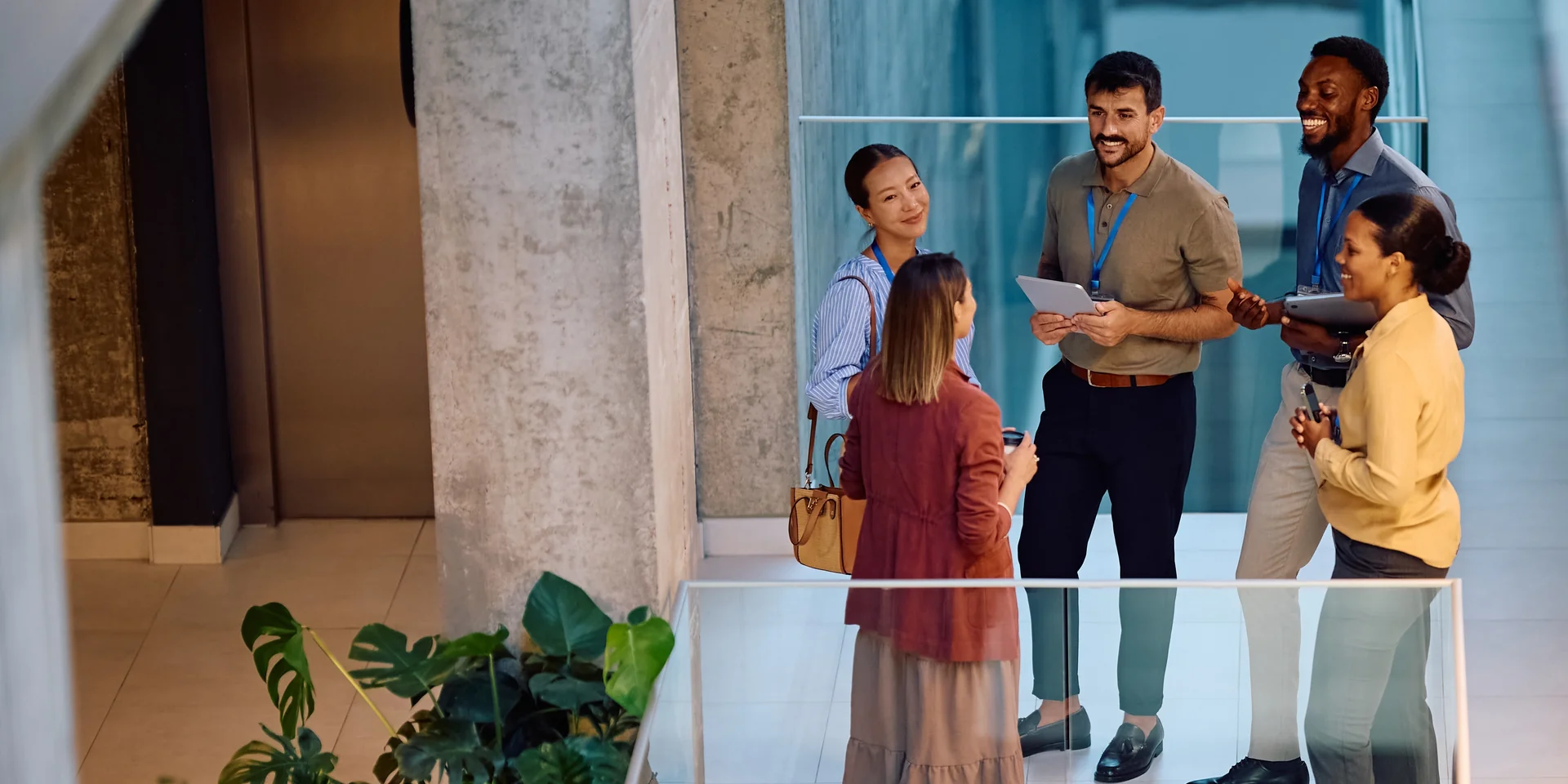 Five colleagues standing in conversation in a bright modern office atrium